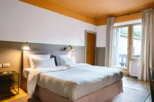 Un letto accogliente in una moderna camera d'albergo dell'HENRI Hotel Garmisch-Partenkirchen con accesso al balcone sullo sfondo.